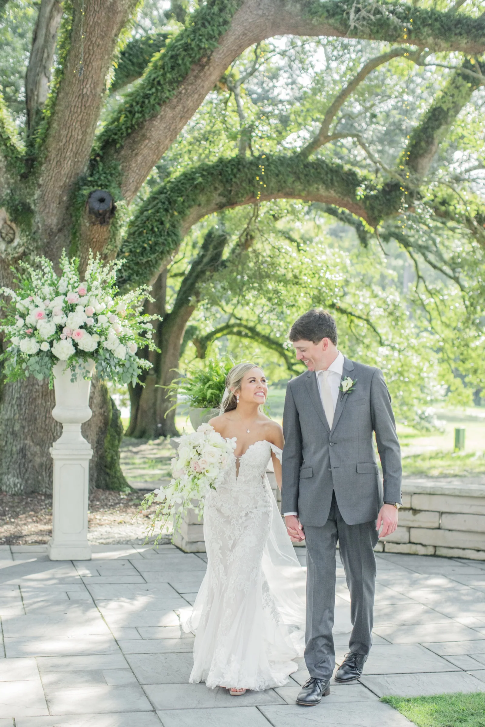Bride and groom holding hands beneath a moss-draped live oak — Kinkade's Fine Clothing weddings
